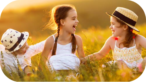 Two girls laughing with little brother in a field of high growth.