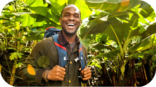 Man smiling at camera standing amongst thick foliage.